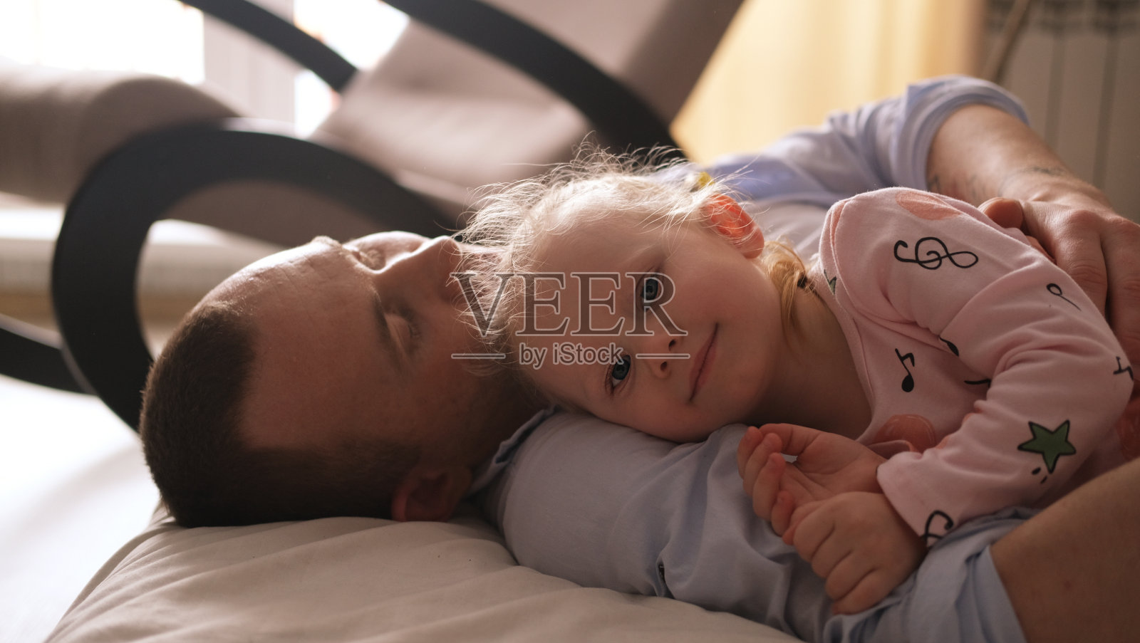 一个笑着的小孩，一个金发的学龄前儿童，在玩彩色的立方体，坐在地板上，穿着粉红色的睡衣，在一个阳光充足的房间里，家里有一个大窗户。儿童的早期发育。照片摄影图片