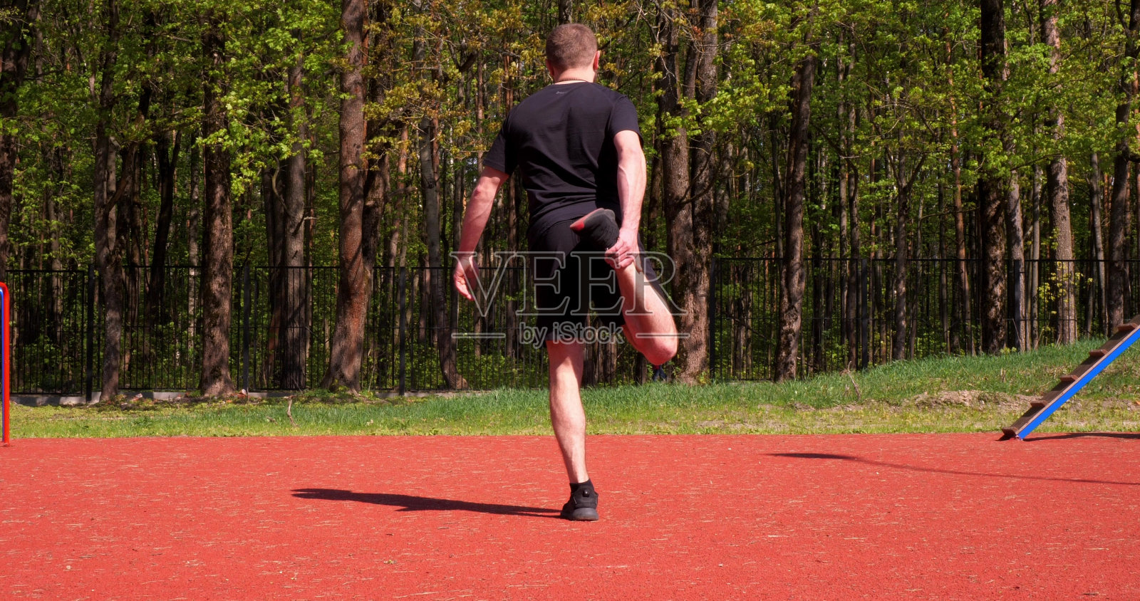 一名男子在运动训练前做热身，背对着镜头站着。一名男子在开始锻炼前做腿部肌肉伸展运动。运动男人的概念。照片摄影图片