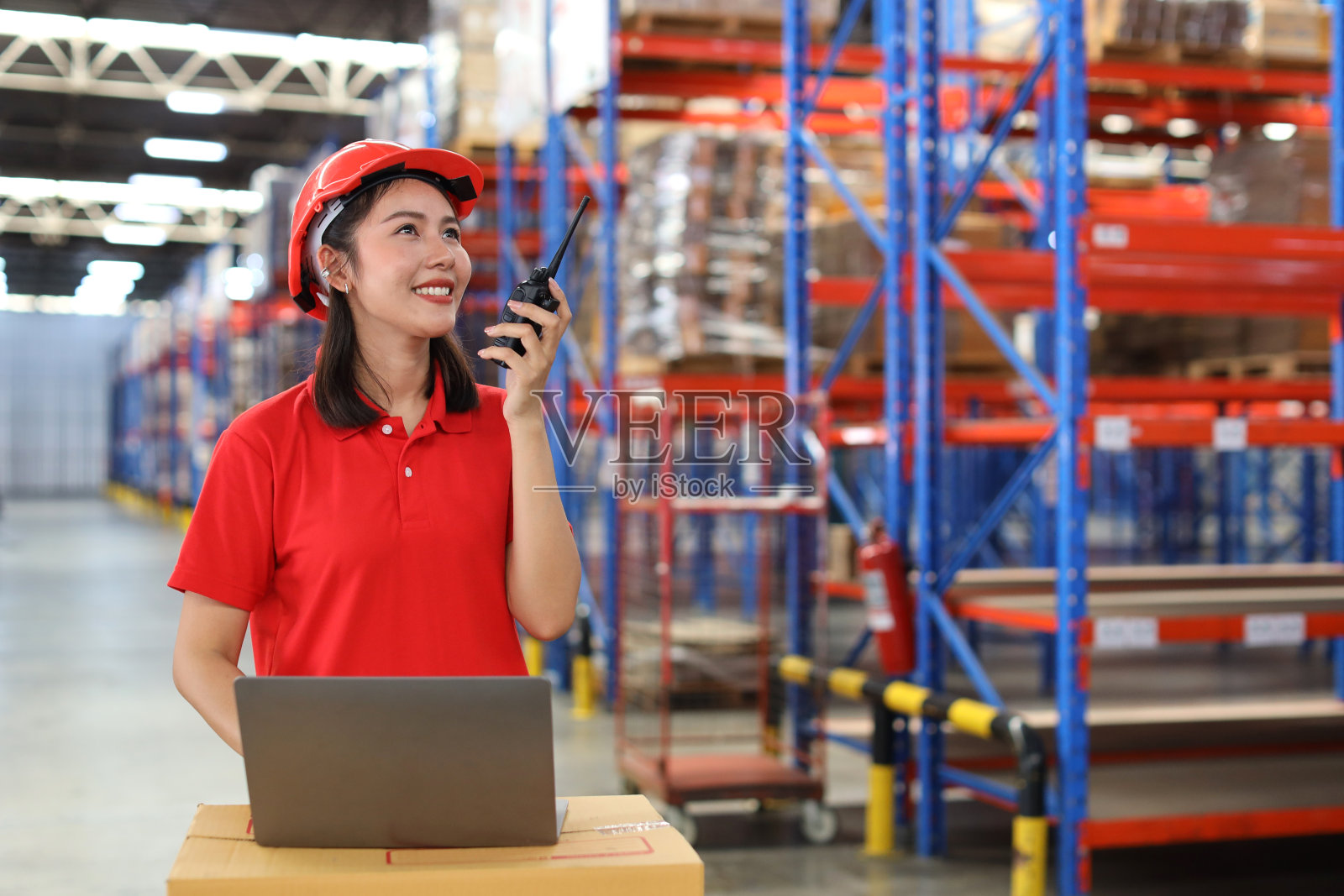 仓库工人年轻的亚洲妇女使用电脑和对讲机收音机，同时控制库存和库存的零售仓库物流，配送中心照片摄影图片