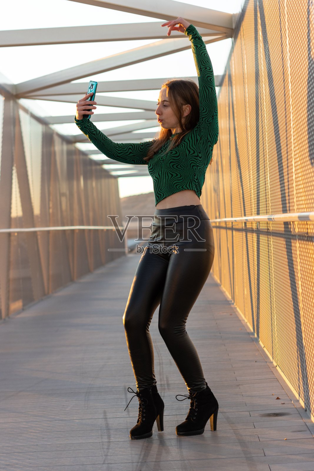 快乐的年轻女子在日落时分在街上用手机跳舞和自拍。垂直的肖像照片摄影图片