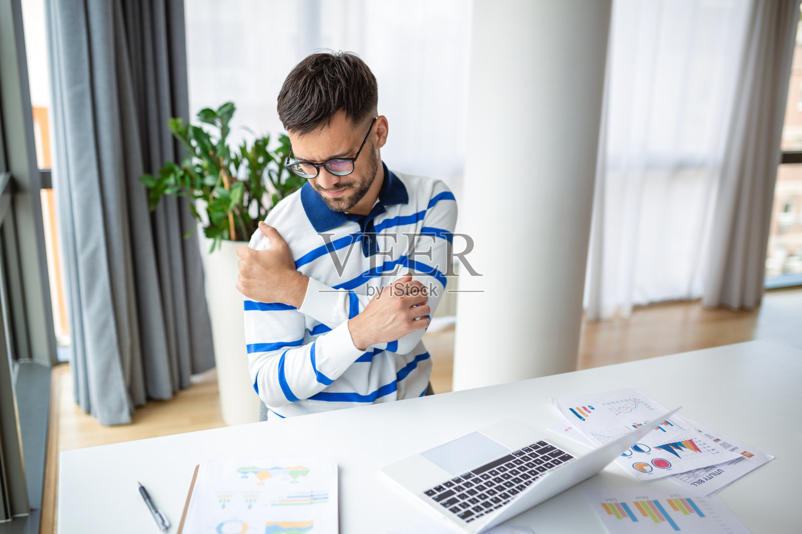 年轻的商人加班工作，在家里使用笔记本电脑时感到肩膀疼痛照片摄影图片
