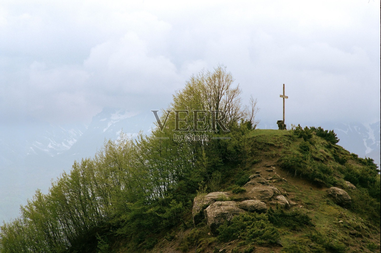在Abruzzo国家公园，一个孤立的十字架坐落在岩石山坡上，周围环绕着茂密的树木照片摄影图片