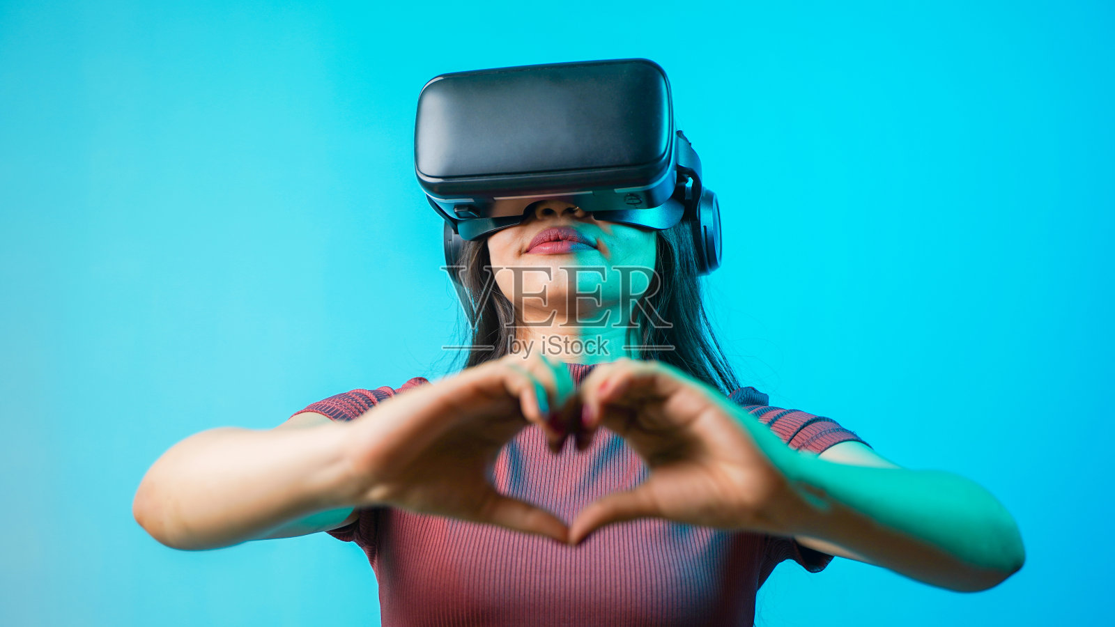年轻的亚洲印度女子手持心形的手，戴着虚拟现实耳机，一个女孩带着vr眼镜的概念工作室肖像照片摄影图片