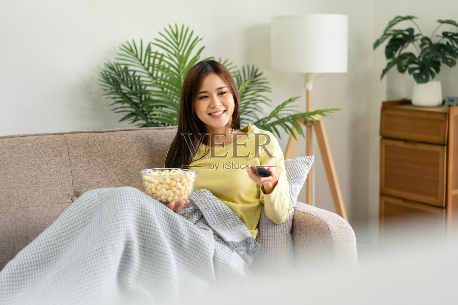 年轻的亚洲妇女正在电视上看电影，手里拿着筷子照片摄影图片