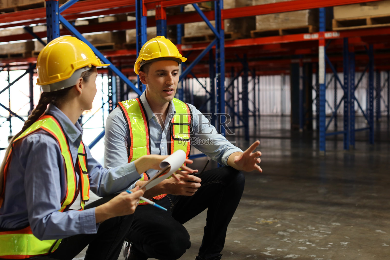一组仓库工人，戴安全帽，穿着反光夹克，使用平板电脑，对讲机和纸板，同时控制零售仓库物流，配送中心的库存和库存照片摄影图片