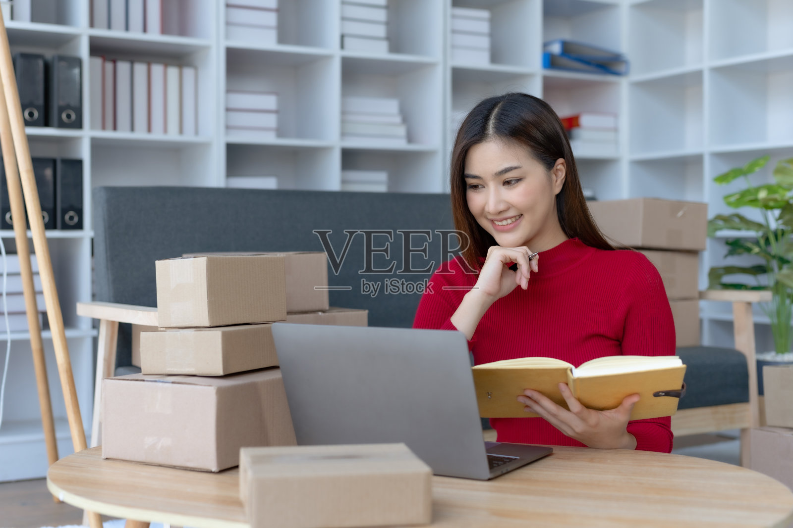 微笑的年轻亚洲女企业主准备包裹箱，在家里的笔记本电脑上检查产品的在线订单。网上购物概念。创办中小企业。照片摄影图片