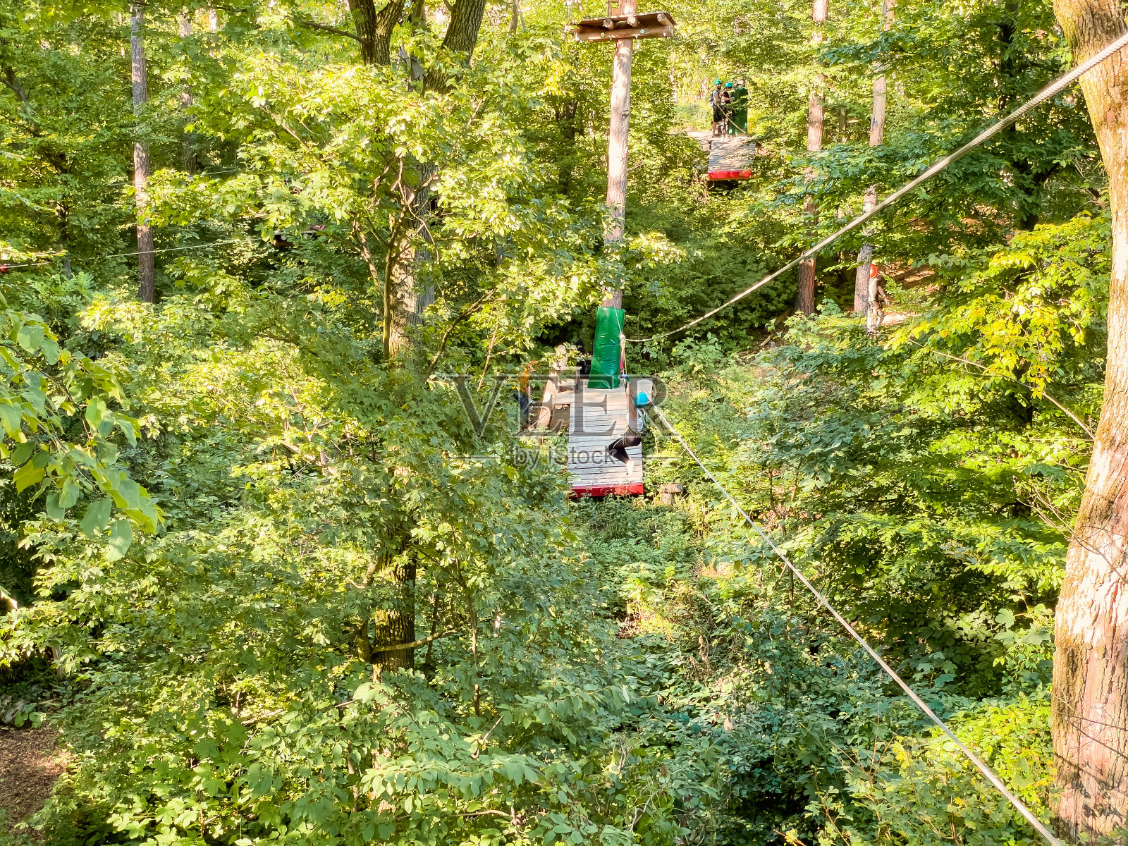 夏季的乐趣和运动冒险的人。冒险公园特写。木林中的绳索公园。在游乐园里，人们戴着安全装备和头盔走在树间的绳桥上。在冒险赛道上进行高海拔攀岩训练照片摄影图片