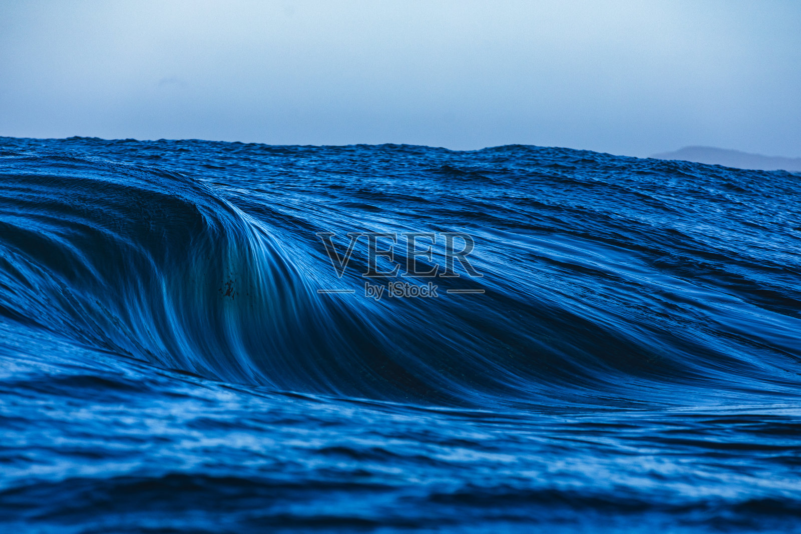 在晴朗晴朗的天气里，一个巨大的蓝色海浪在礁石上形成照片摄影图片