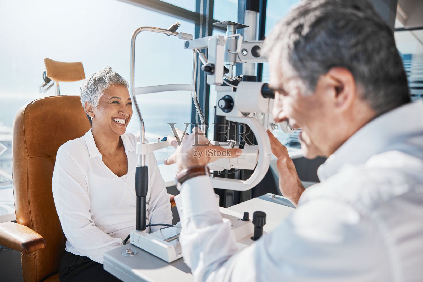 眼科医生、机器或快乐的女人在验光师那里咨询视力帮助。验光师与资深客户交谈或询问有关视力、虹膜或视网膜健康测试的信息照片摄影图片