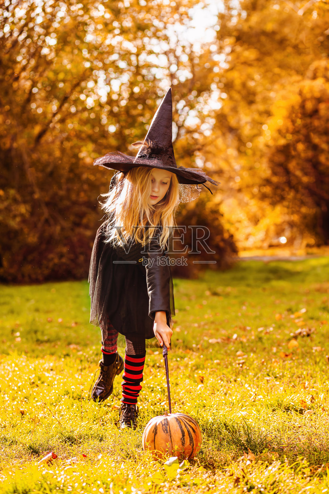 一个穿着女巫服装的女孩念了一个咒语，用魔杖给南瓜施了魔法照片摄影图片