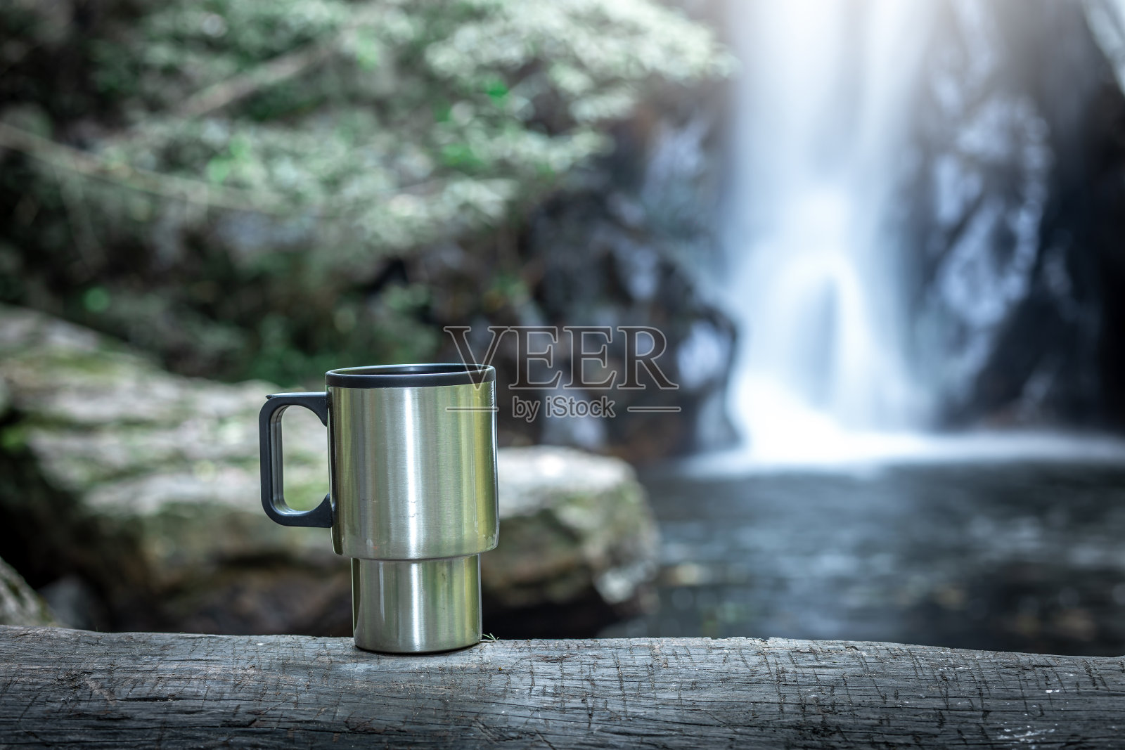 木头上的铁制咖啡杯，背后是瀑布。照片摄影图片
