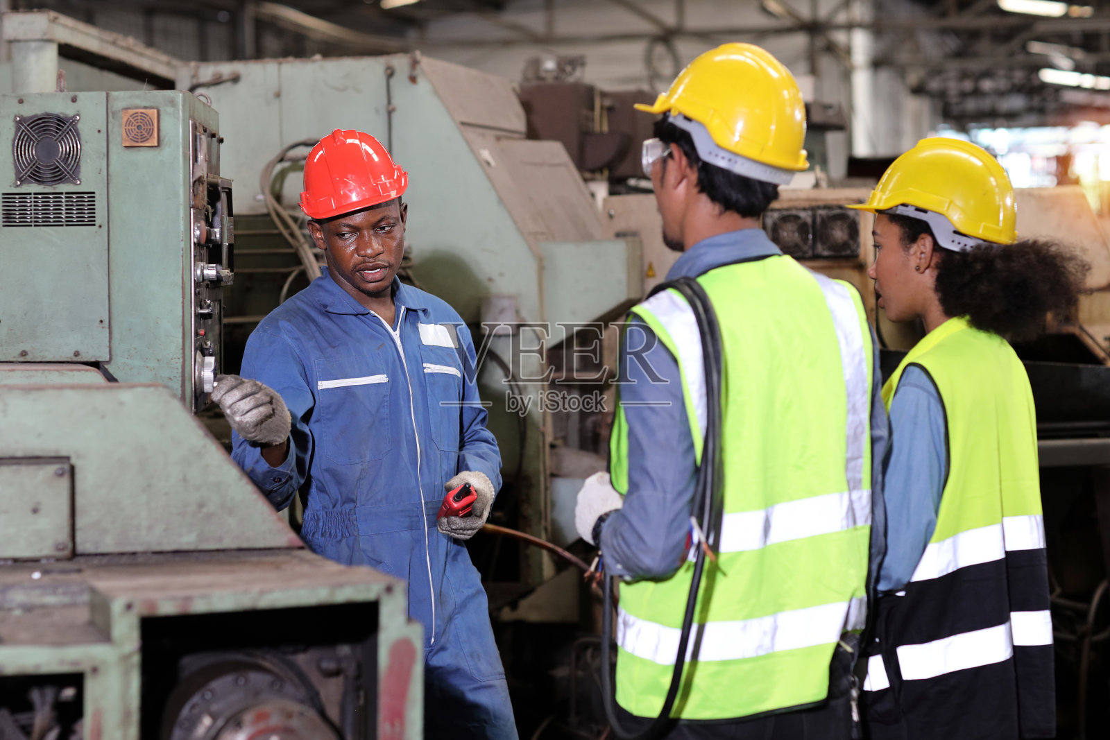 在重工业制造工厂，穿着防护服，戴着安全帽，教学徒或同事使用计算机控制机器的技术工程师照片摄影图片