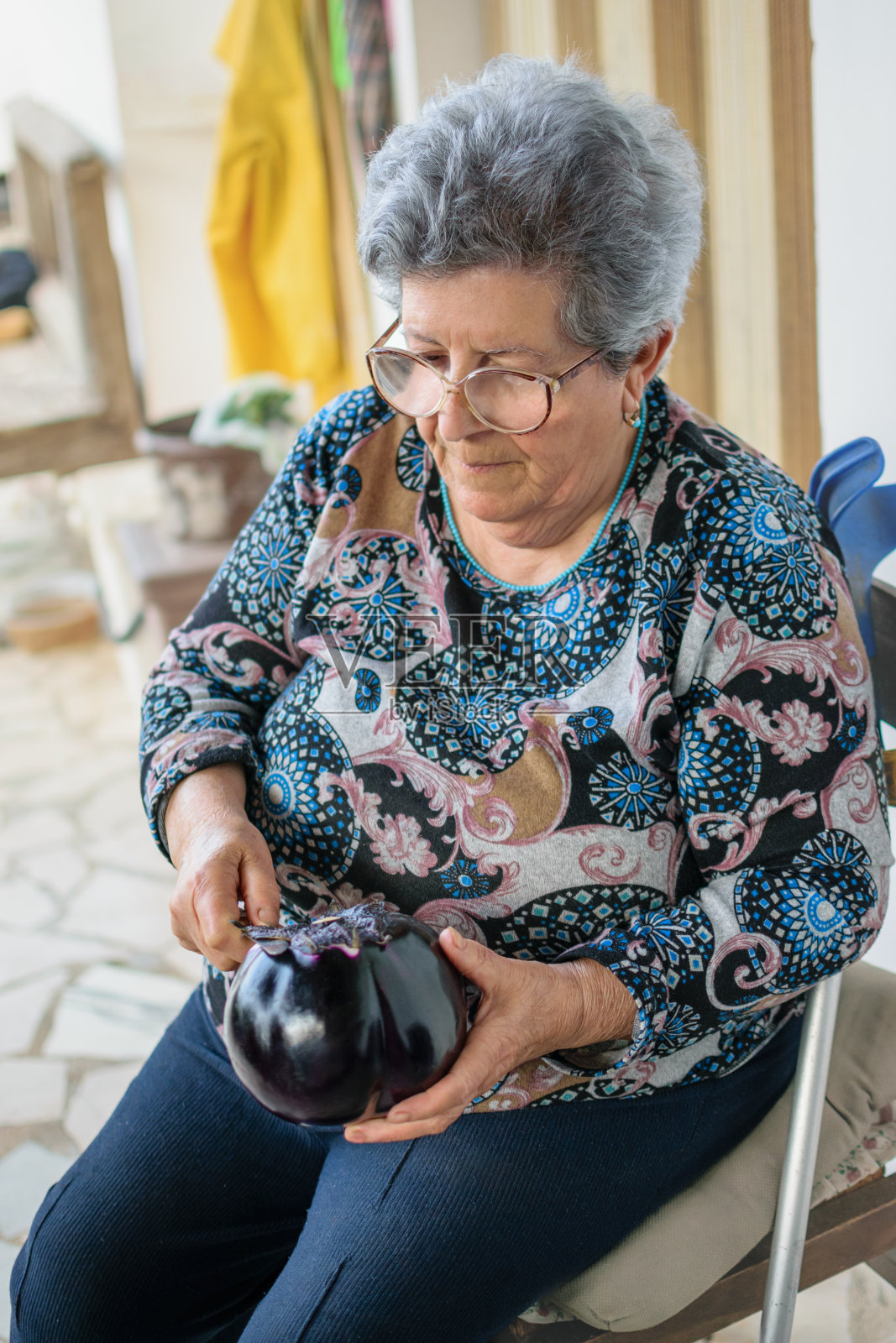 一位老妇人坐在自家花园的露台上剥茄子照片摄影图片