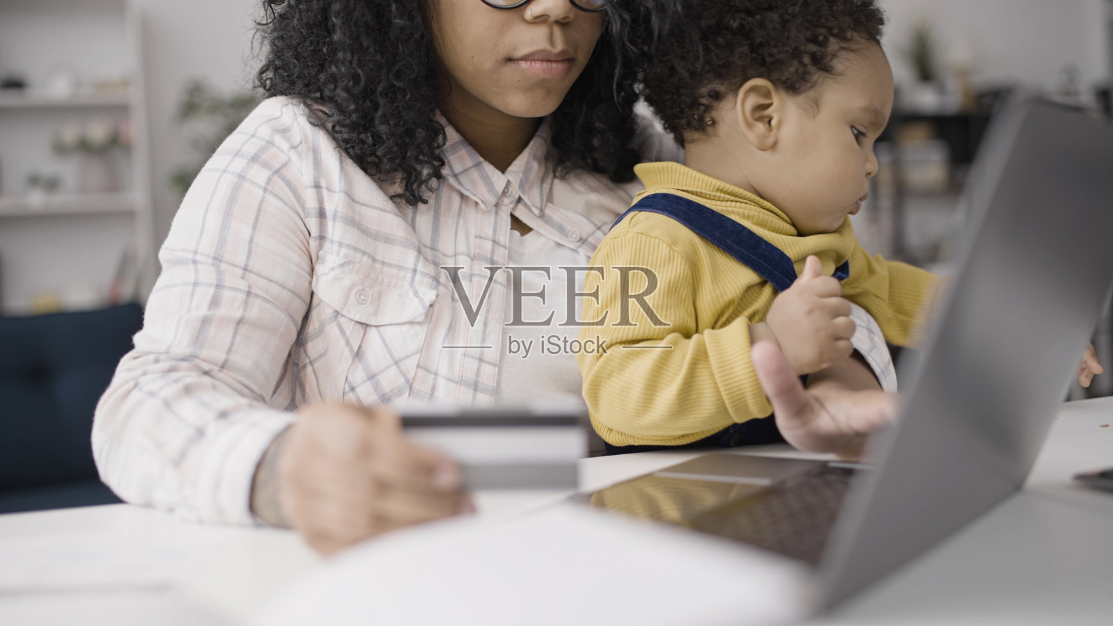 忙碌的妈妈膝上抱着孩子，输入信用卡号码，在网上订购食物和商品照片摄影图片