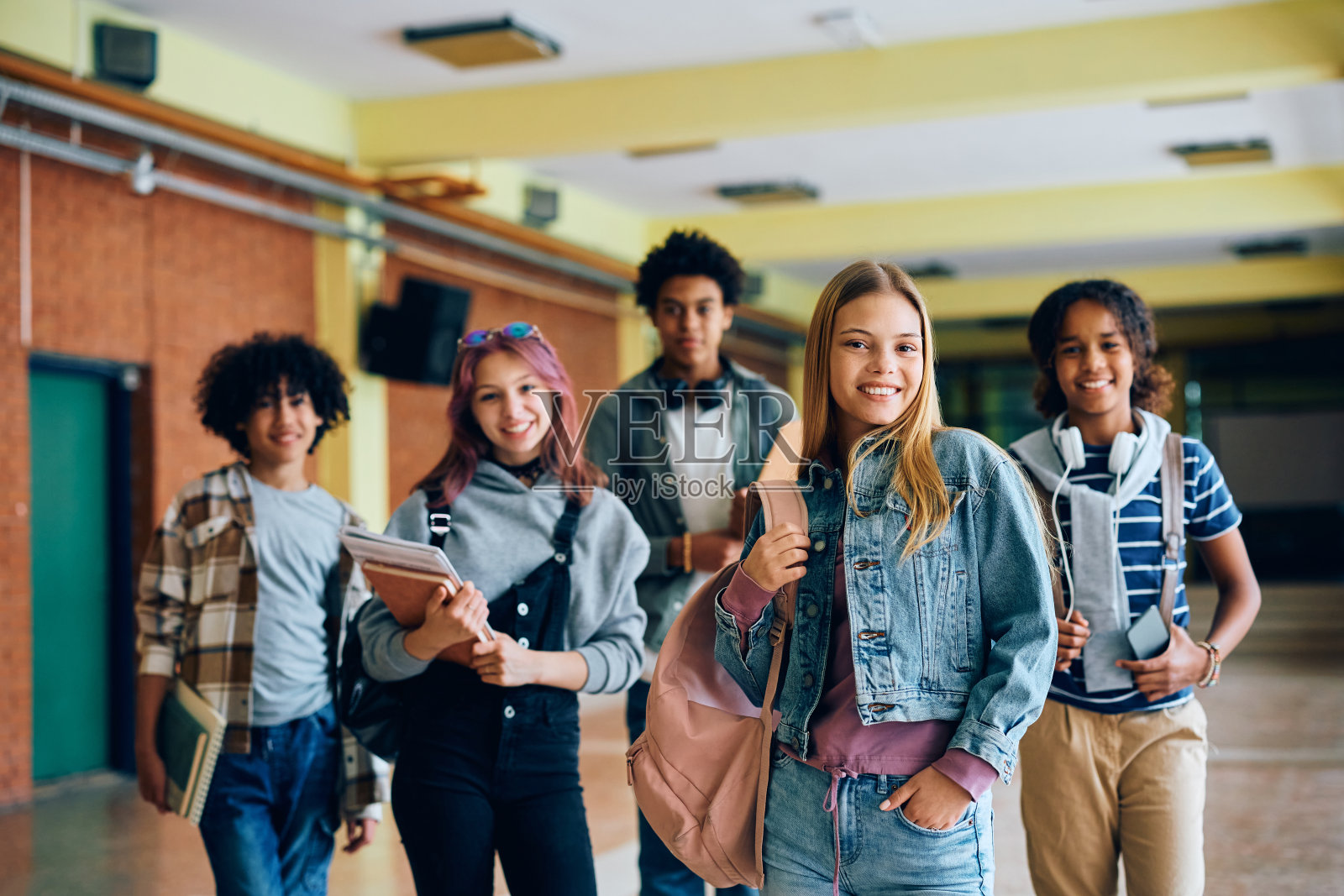 快乐的少女和她的朋友在高中走廊看着相机。照片摄影图片
