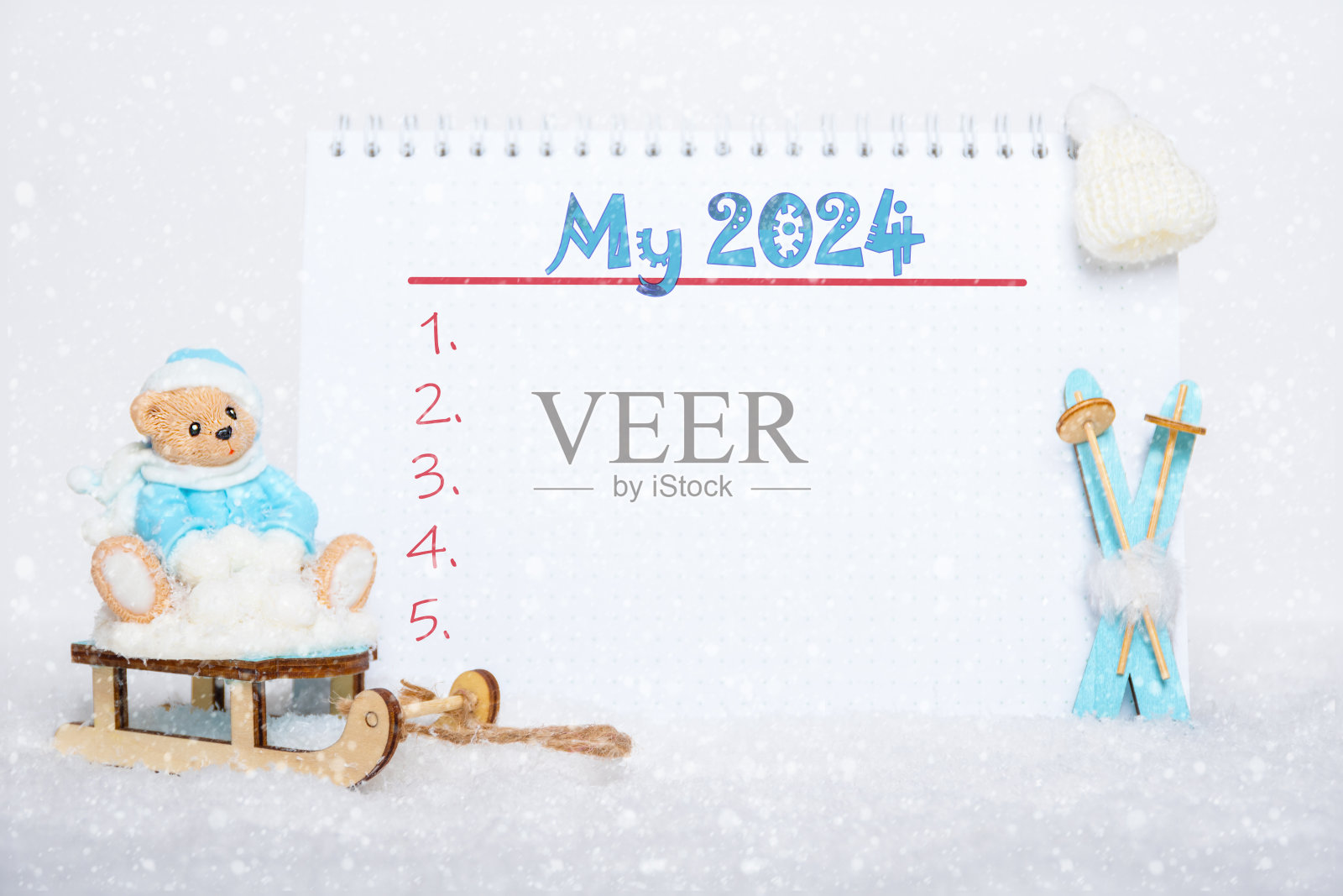 新年目标清单。泰迪熊坐在雪橇上，滑雪板上，戴着一顶白帽子，还有一本写着“我的2024”的笔记本照片摄影图片