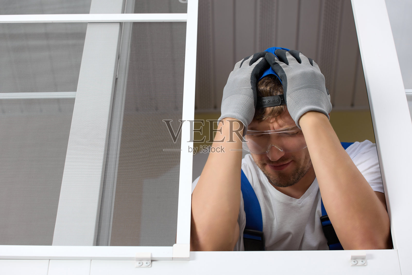 戴着眼镜和手套的安装人员惊慌地把头靠在开着的窗户前照片摄影图片
