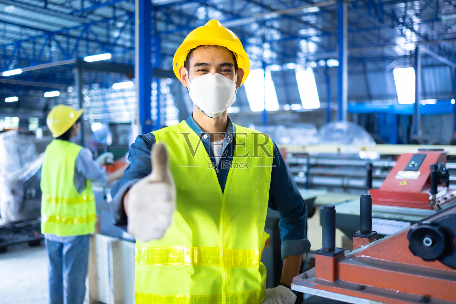 工厂里的亚洲工人正在使用和正在工作的工业工程师合作伙伴看着相机，微笑着。戴安全帽的工程师在工作和检查机器。照片摄影图片