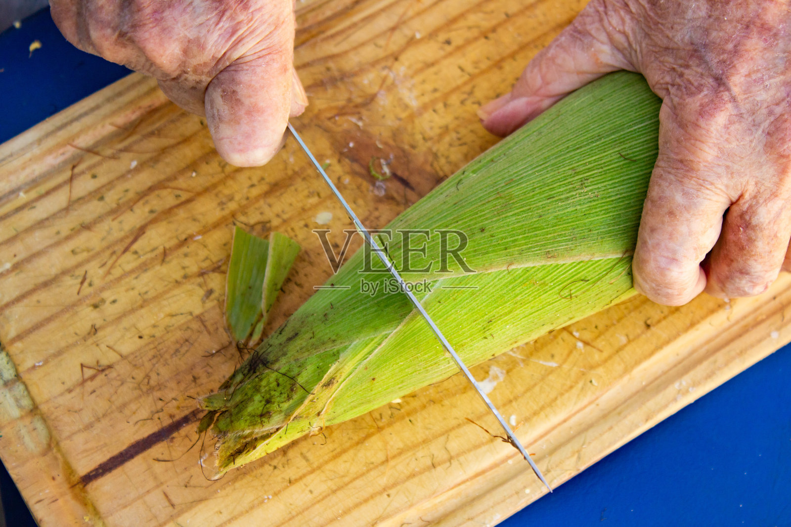 一位女士的手正在切玉米棒的尖端。照片摄影图片
