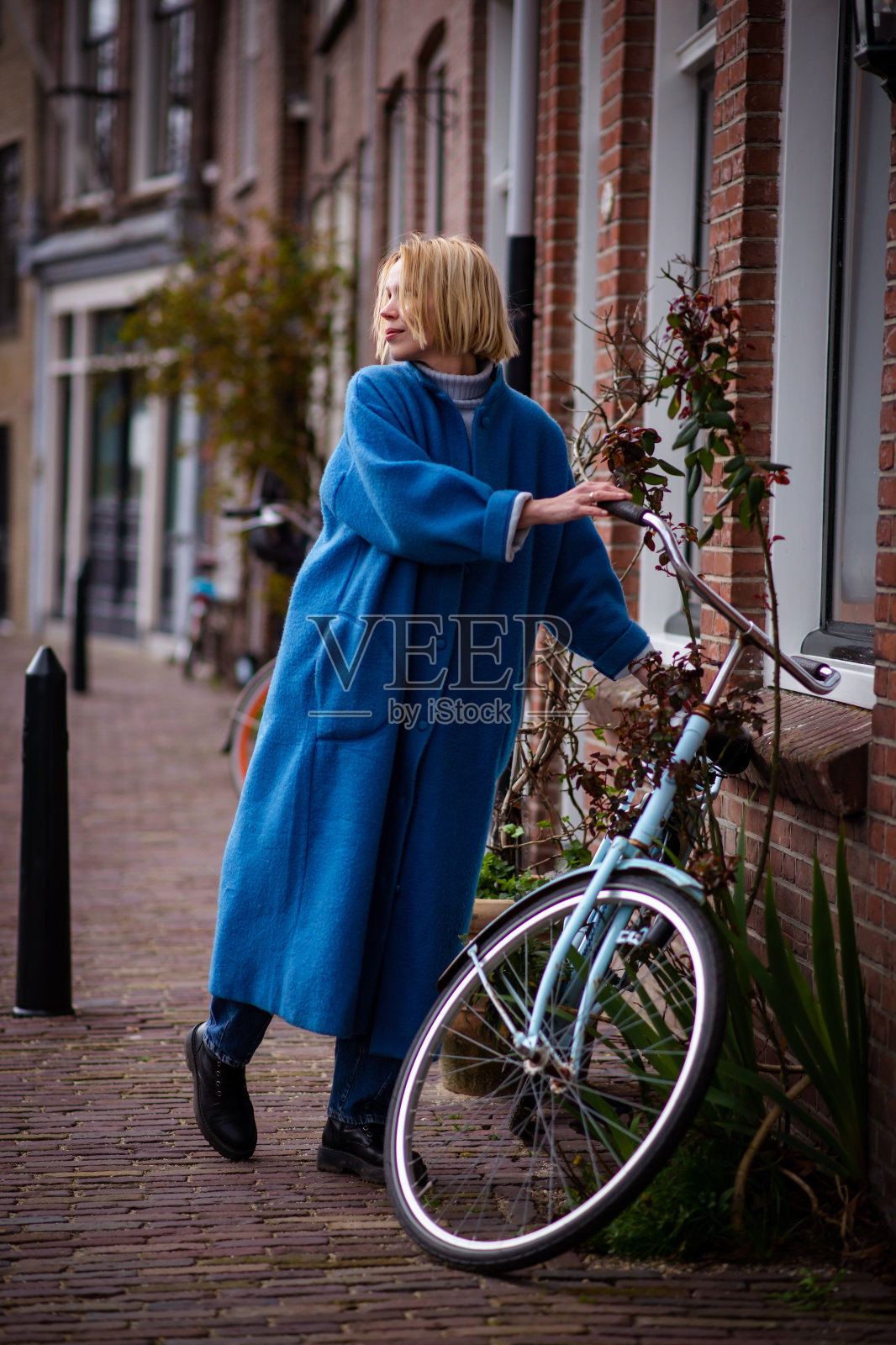 荷兰一位身穿蓝色长外套的妇女。游客在鹿特丹旅游时。一个成年妇女骑自行车。照片摄影图片