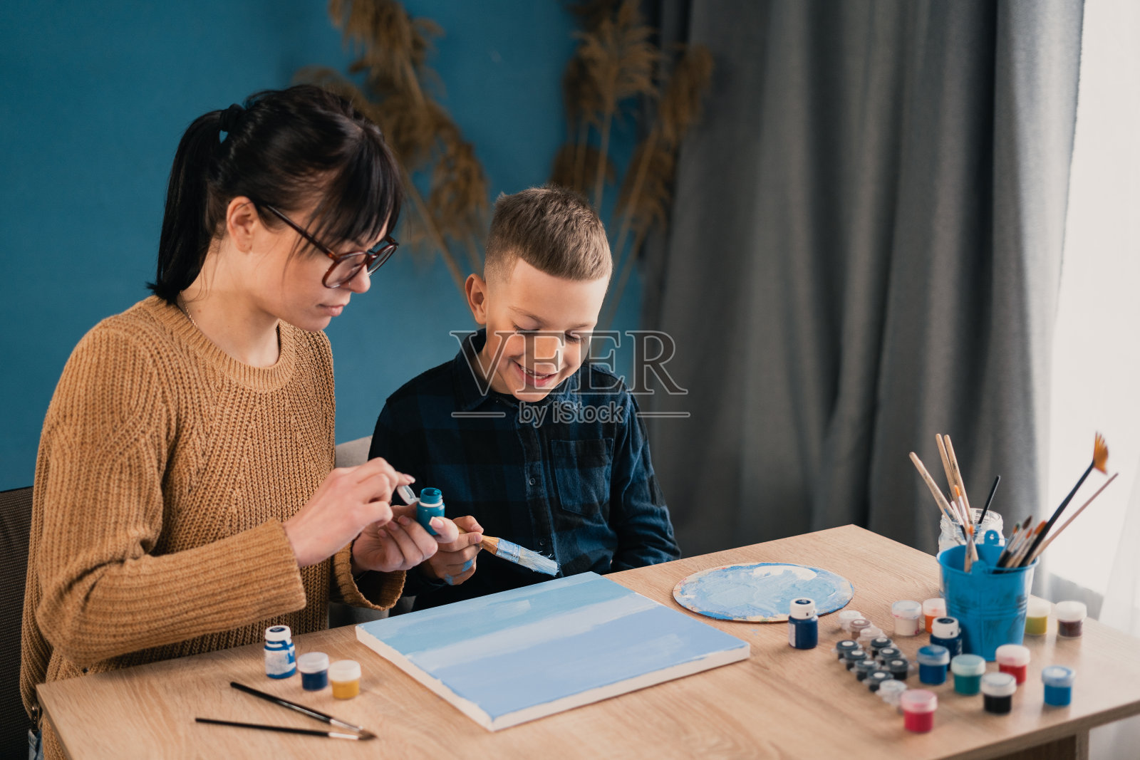 一个年轻漂亮的女人教她的学生儿子在家里用油画颜料在画布上画画。一个女人花时间陪她的孩子照片摄影图片
