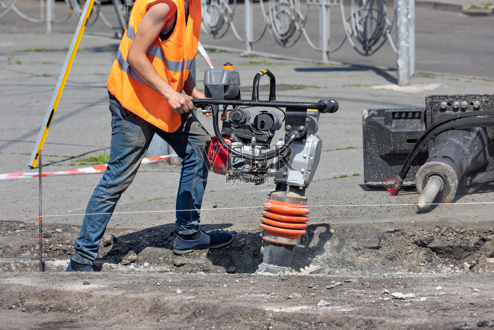在一个阳光明媚的夏日，一名建筑工人正在用振动夯夯土。照片摄影图片