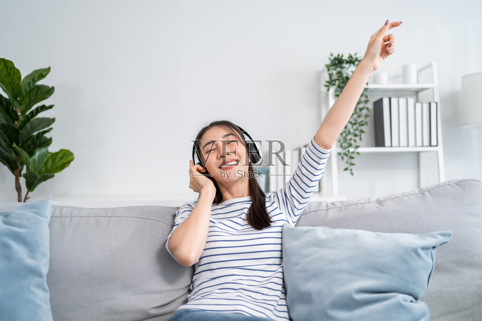 亚洲妇女坐在沙发上听音乐和跳舞。迷人美丽的年轻女孩戴上耳机，开心地在家度过闲暇时光，享受周末在家的活动。照片摄影图片