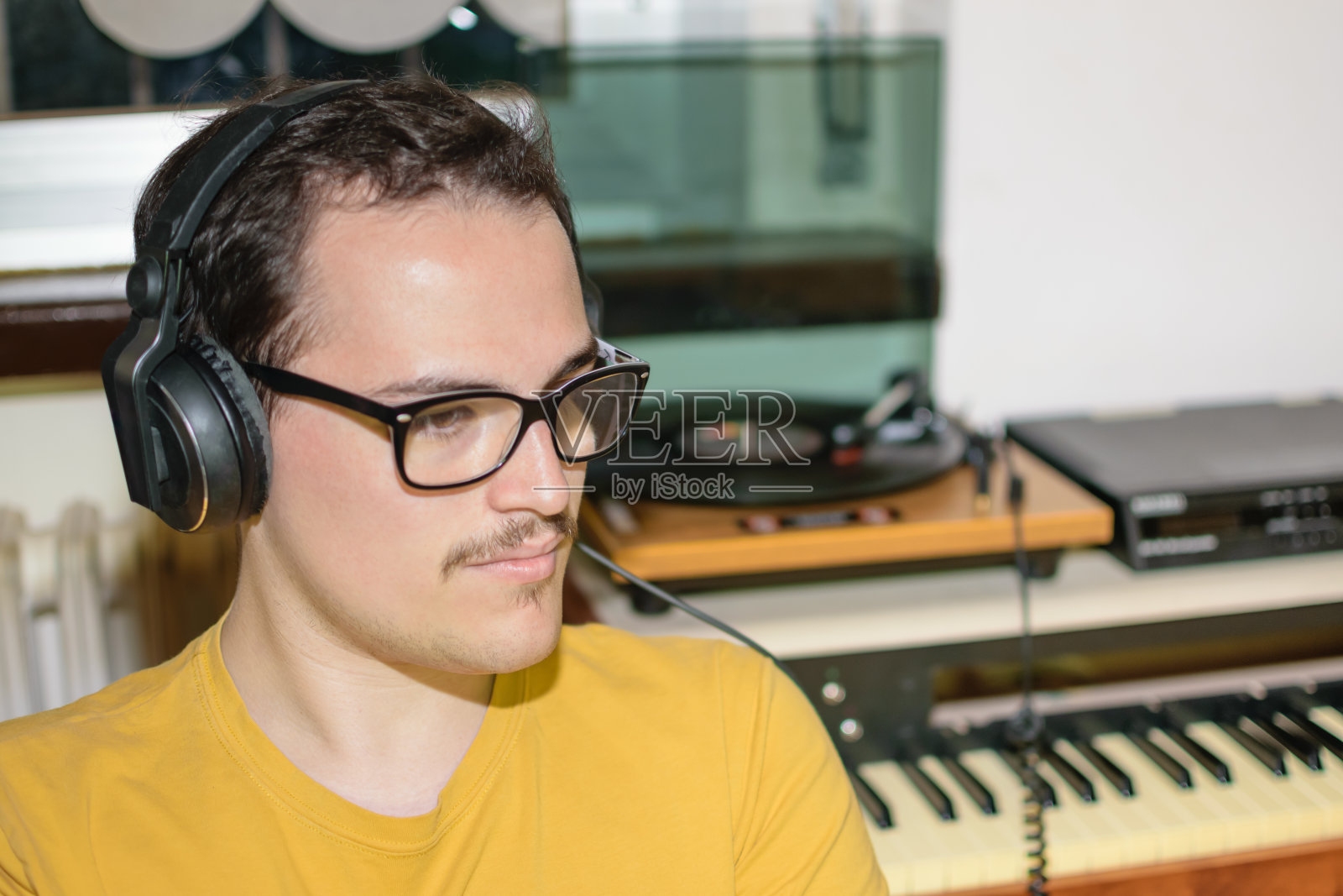 戴着眼镜的年轻人在房间里用老式耳机听着黑胶唱片照片摄影图片