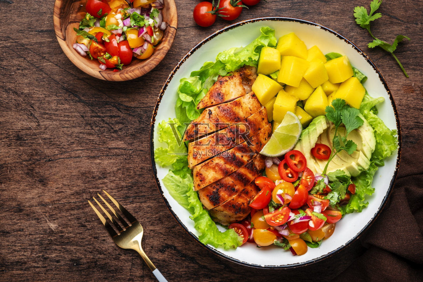 烤鸡配以牛油果、芒果、番茄沙司、香菜、酸橙和生菜制成的配菜沙拉，质朴的木制餐桌背景，俯视图照片摄影图片