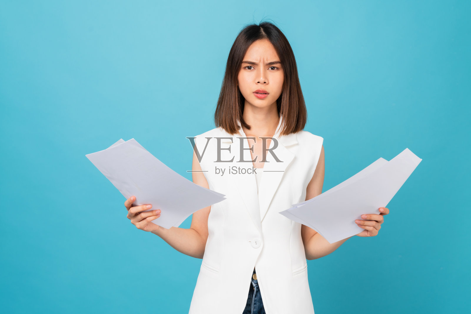 无聊的年轻亚洲女人拿着文件，站在工作室拍摄的蓝色背景上。照片摄影图片