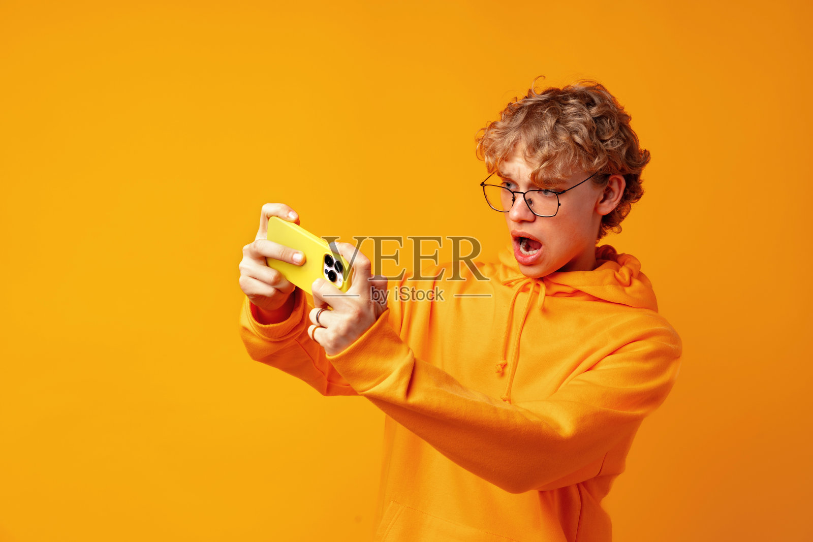 年轻人在手机上玩网络游戏的照片，背景是黄色照片摄影图片