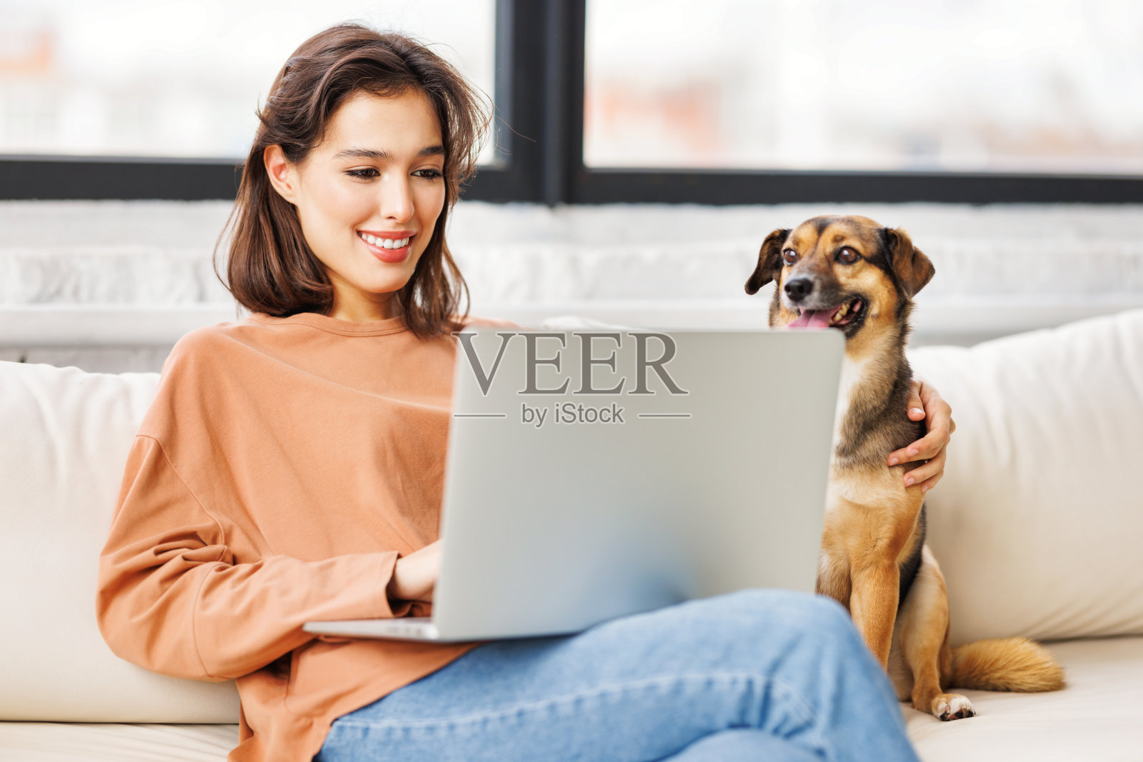 快乐的女性自由职业者在家里远程用笔记本电脑和宠物狗一起工作照片摄影图片