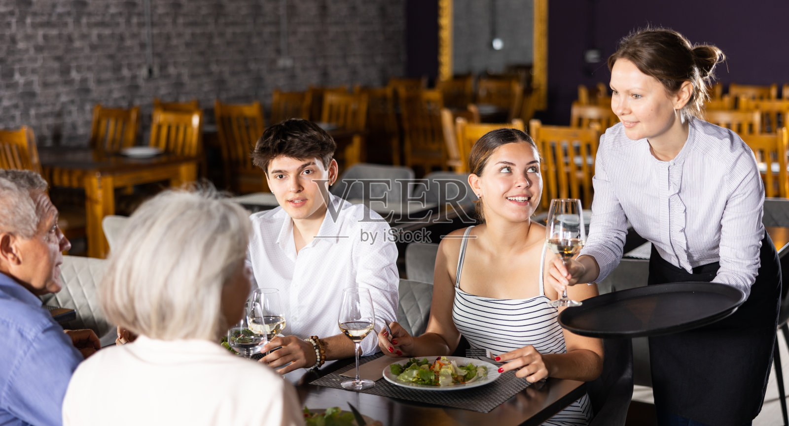 友好的女服务员给老夫妇和年轻夫妇端来了一杯酒照片摄影图片