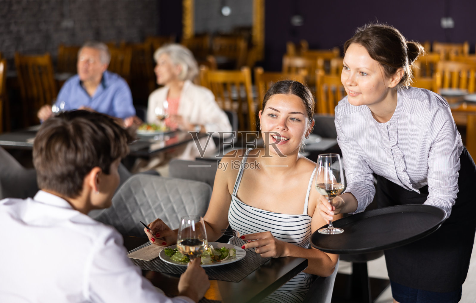 女服务员为坐在餐厅餐桌旁的年轻夫妇端上饮料照片摄影图片