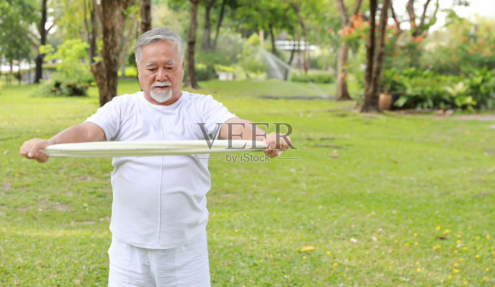 亚洲老年男性退休后在公园户外用毛巾做瑜伽、太极、伸展、冥想等放松健康的运动。快乐老年人户外生活理念照片摄影图片