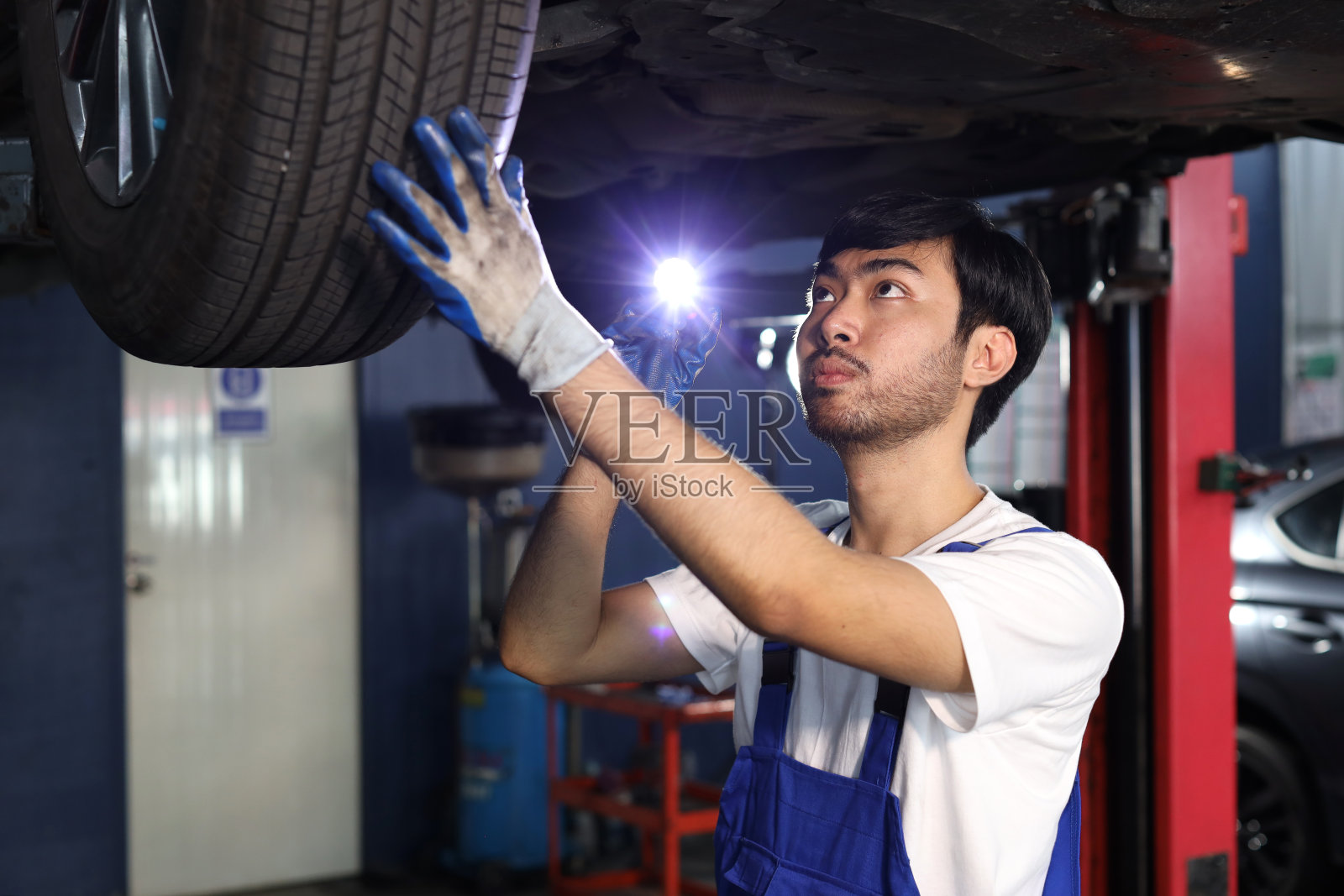 一名穿着制服的汽车技师在维修站检查或维修吊车服务。工人手持扳手，用手电筒固定车辆。汽车维修中心的服务理念照片摄影图片