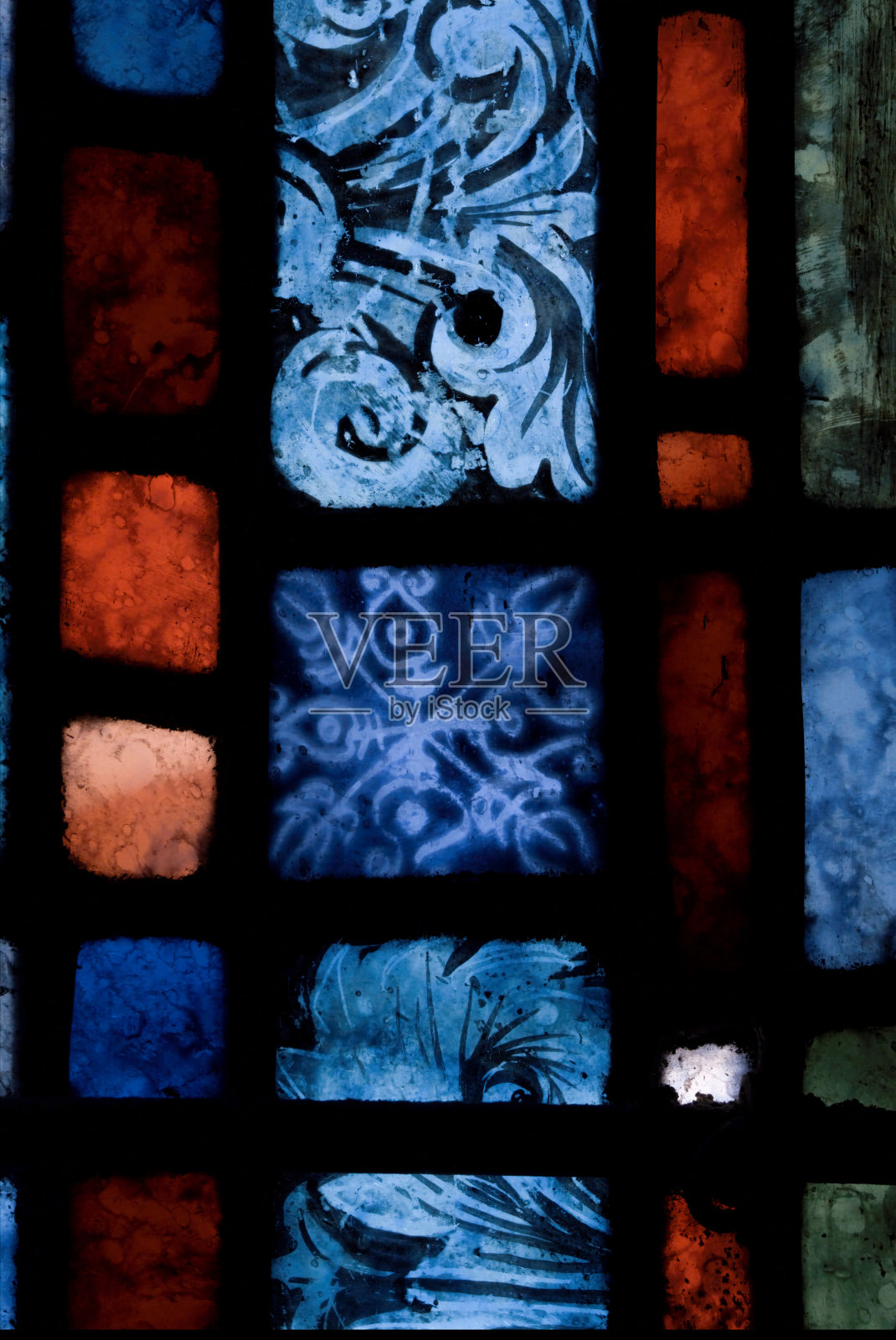 彩色含铅玻璃的近距离细节图像，显示蓝色，红色，绿色的正方形，矩形和绘制的图案细节。中世纪时期。照片摄影图片