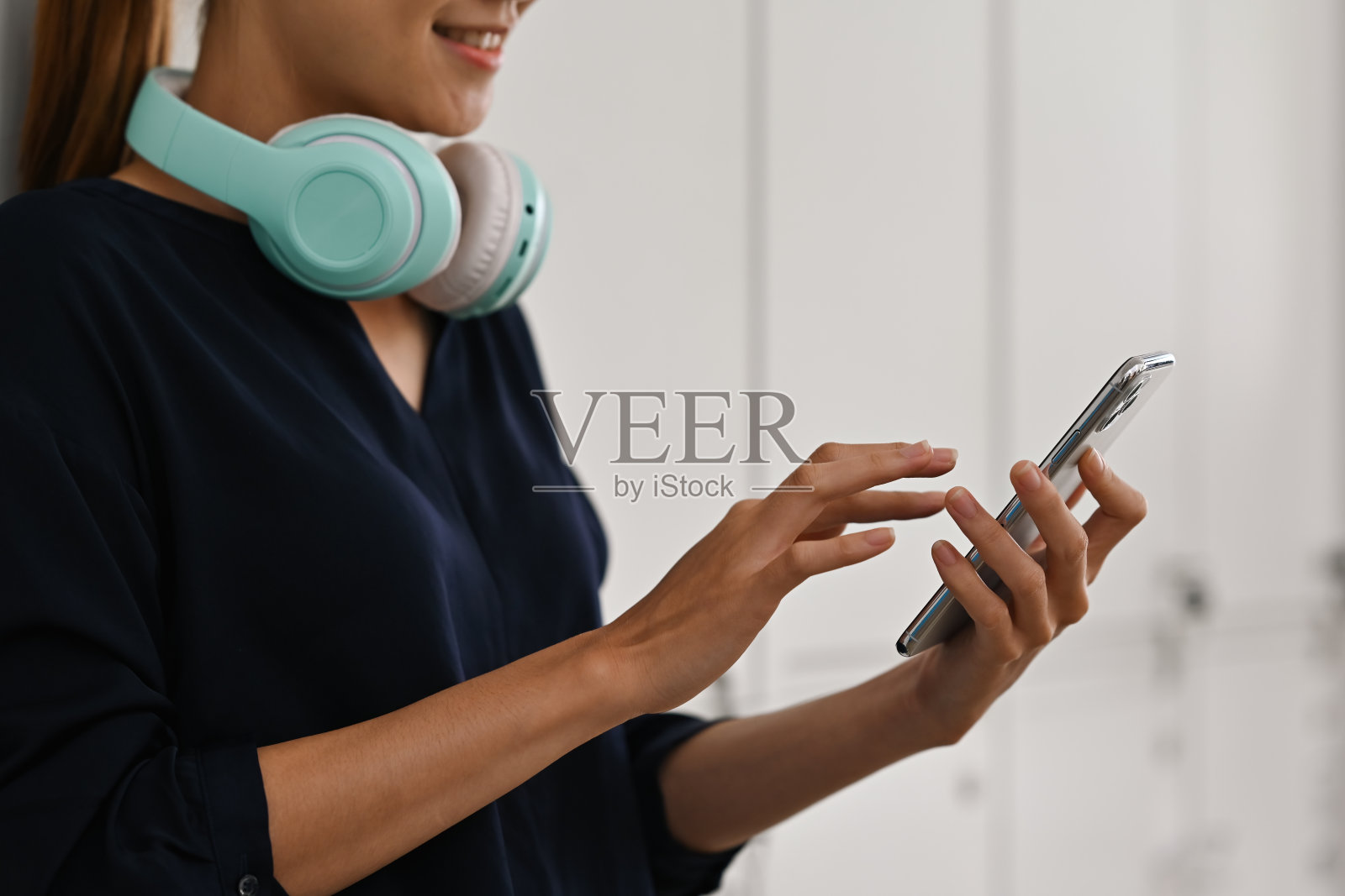 一个年轻的亚洲女性，脖子上挂着耳机，正在使用智能手机。照片摄影图片