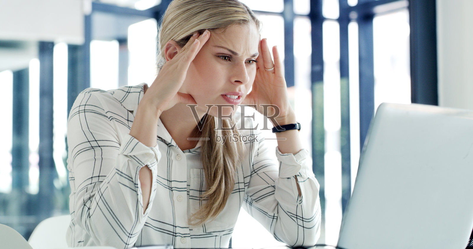 一个女商人在现代办公室里带着压力和头痛使用笔记本电脑。一位在线工作的女商人，在办公桌前感到疲惫不堪照片摄影图片