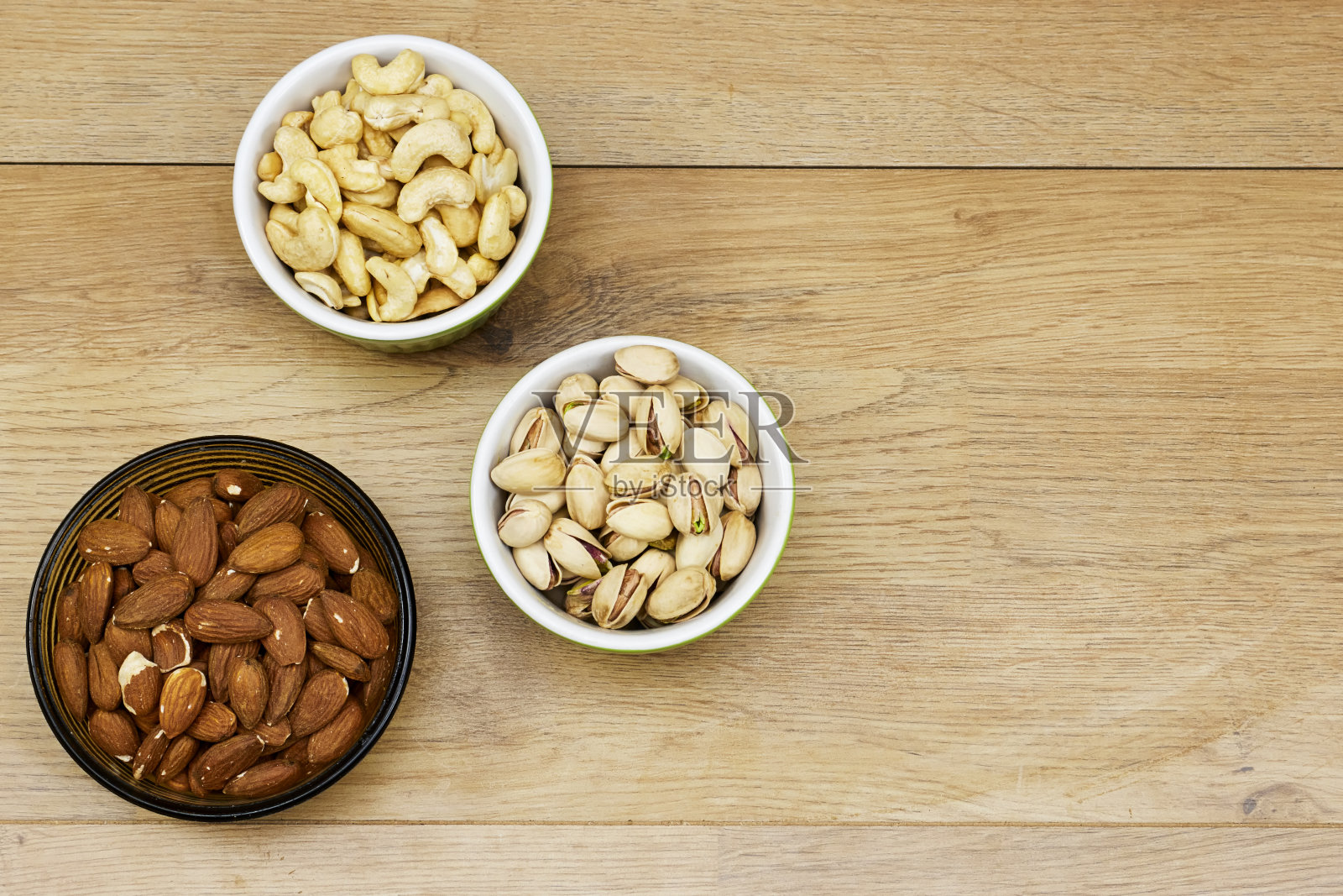坚果(杏仁、开心果、腰果)装在木桌上的碗里照片摄影图片