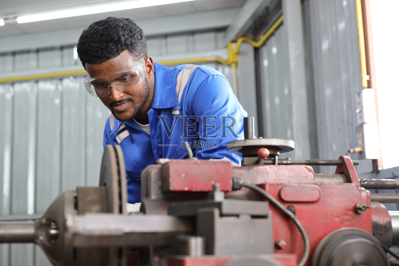 穿着防护服的技师或工人使用金属车床在车库抛光汽车盘式制动器。维护汽车和检查汽车零件的概念照片摄影图片