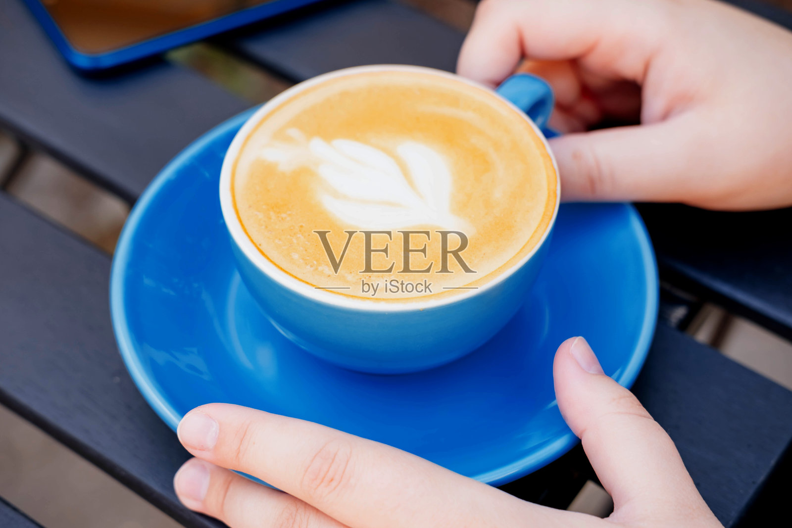 夏日露台上的木桌上，一个女孩手里拿着一杯卡布奇诺。照片摄影图片