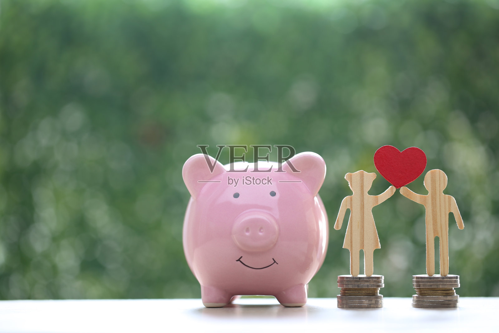 爱的夫妇拿着心形的小猪储蓄罐和一堆硬币，在自然的绿色背景上，为将来的准备和家庭理财的概念存钱照片摄影图片