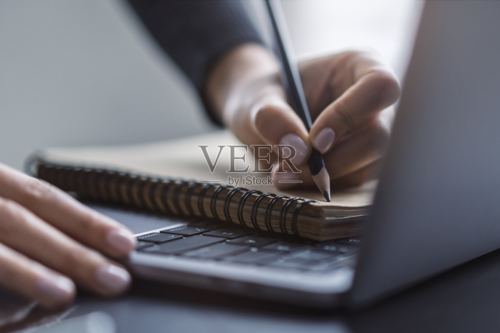 一个女人的手在一个尖端的笔记本电脑上做笔记的细节视图，背景是模糊的照片摄影图片