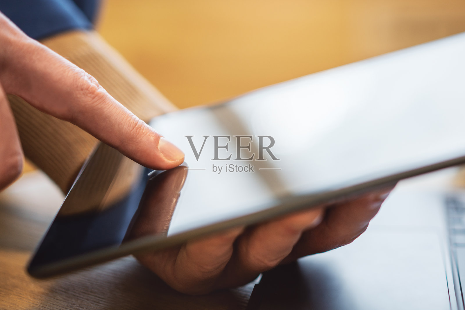 一个男人的手指在桌子上操作高科技平板电脑的特写，在一个明亮的办公室场景的模糊背景中照片摄影图片