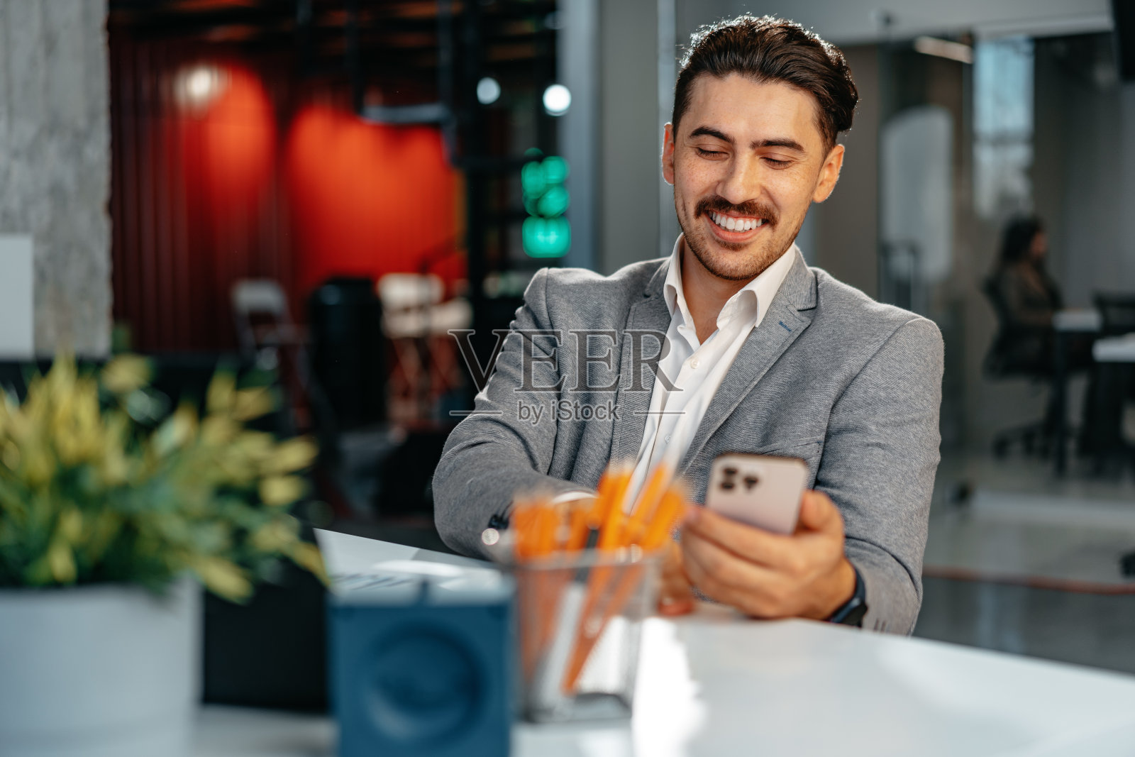 穿着正装的商人坐在工作桌旁玩智能手机照片摄影图片