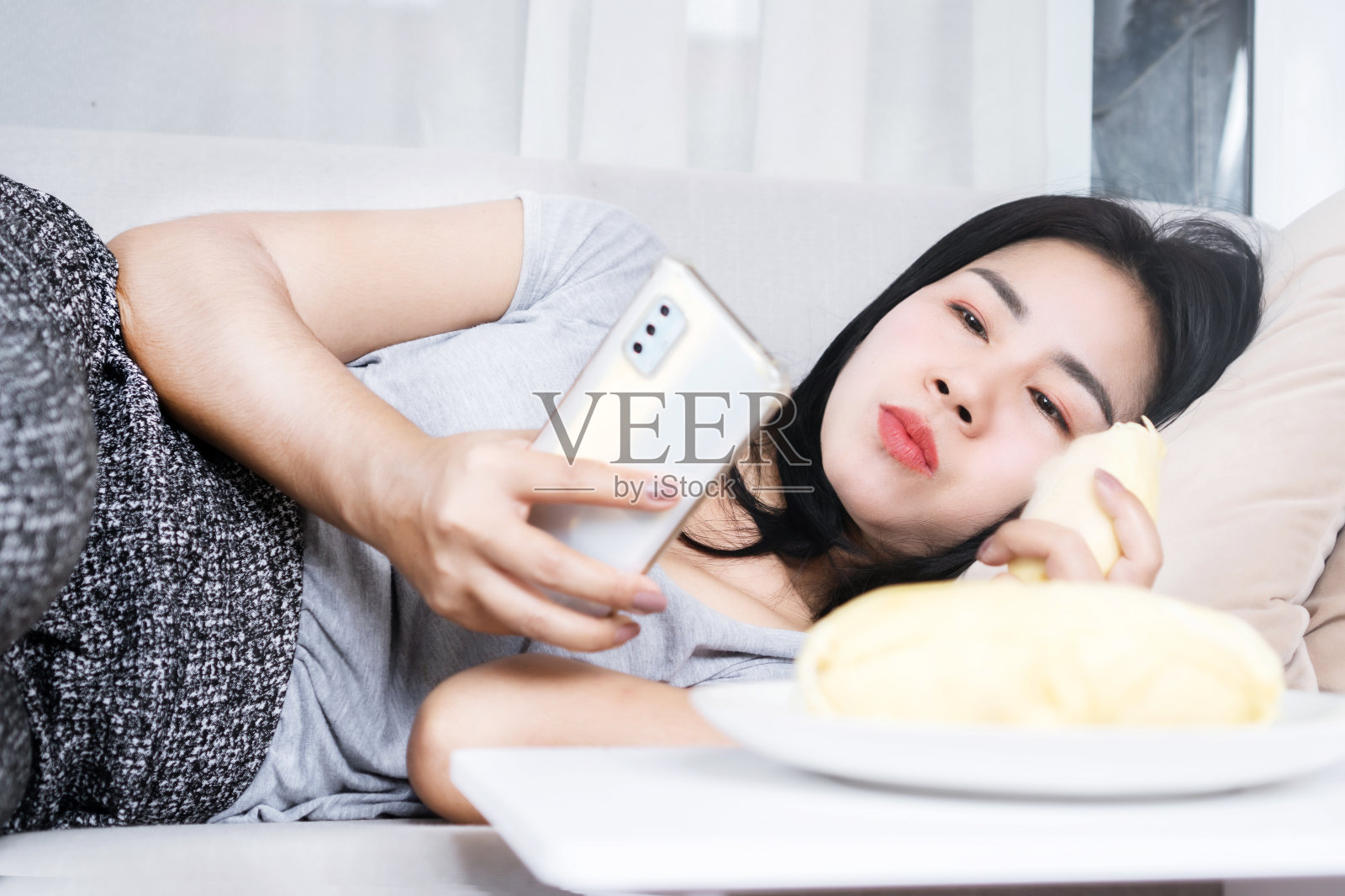 放松的亚洲女性一边玩手机一边吃榴莲，不健康的生活方式照片摄影图片