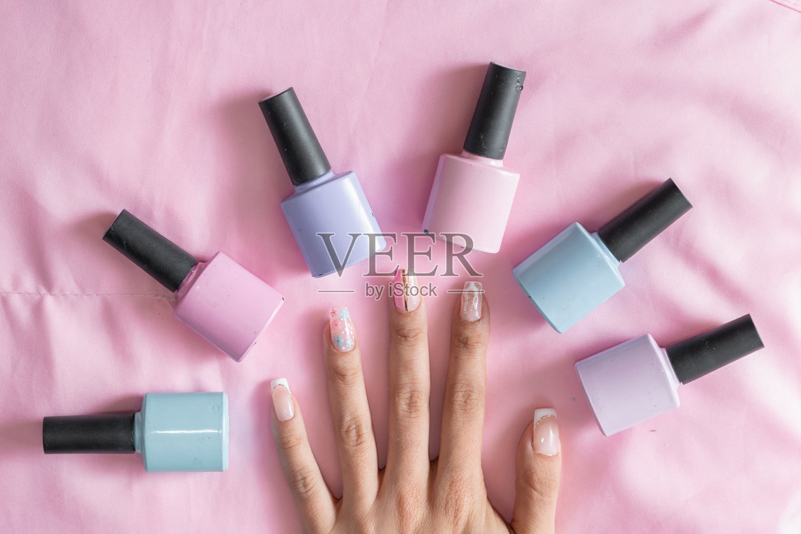 一个女人的手的详细视图，在粉红色的背景上，涂着彩色指甲油的指甲周围照片摄影图片