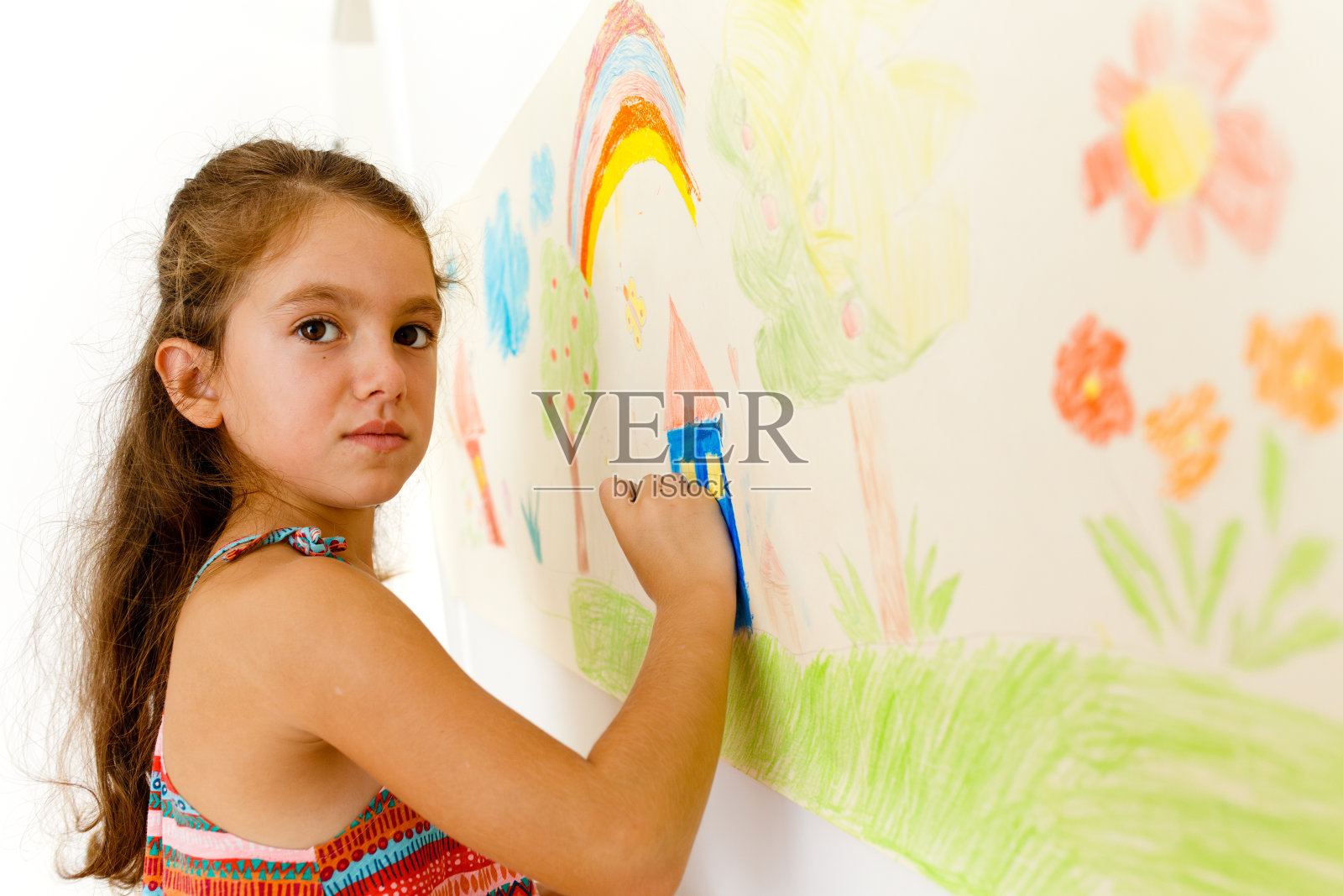 小女孩用蜡笔在粘在墙上的纸卷上画画照片摄影图片