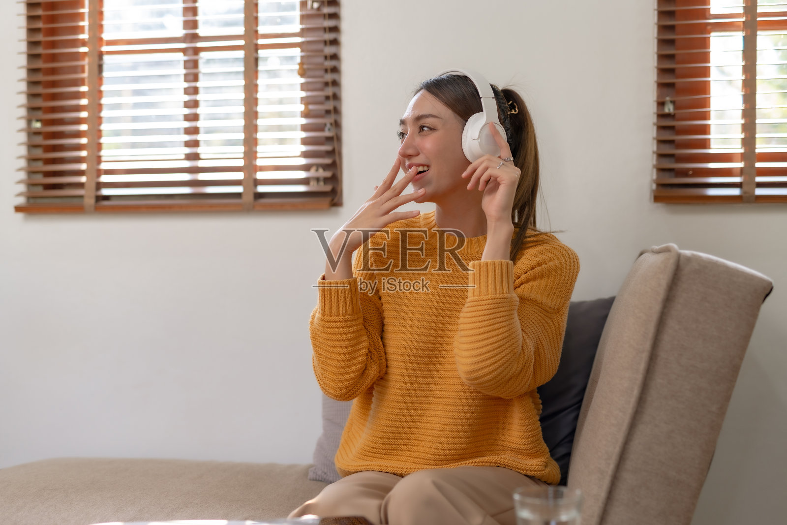 可爱的亚洲年轻女子戴着耳机坐在沙发上听音乐快乐和放松在家听音乐。照片摄影图片